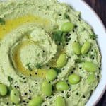 Edamame Hummus with Black and white sesame seeds, garnished with parsley, served in white bowl.