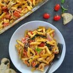 Baked feta pasta in a white bowl, fork and bread on the sides