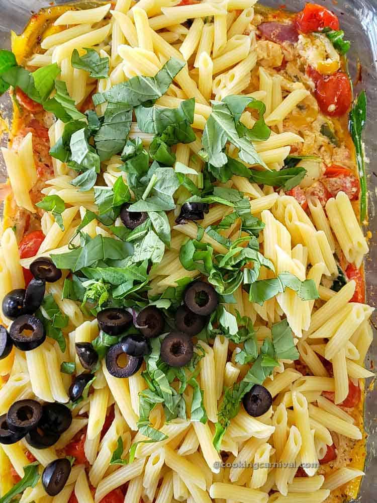 adding pasta, basil, and olives in baked feta and tomato