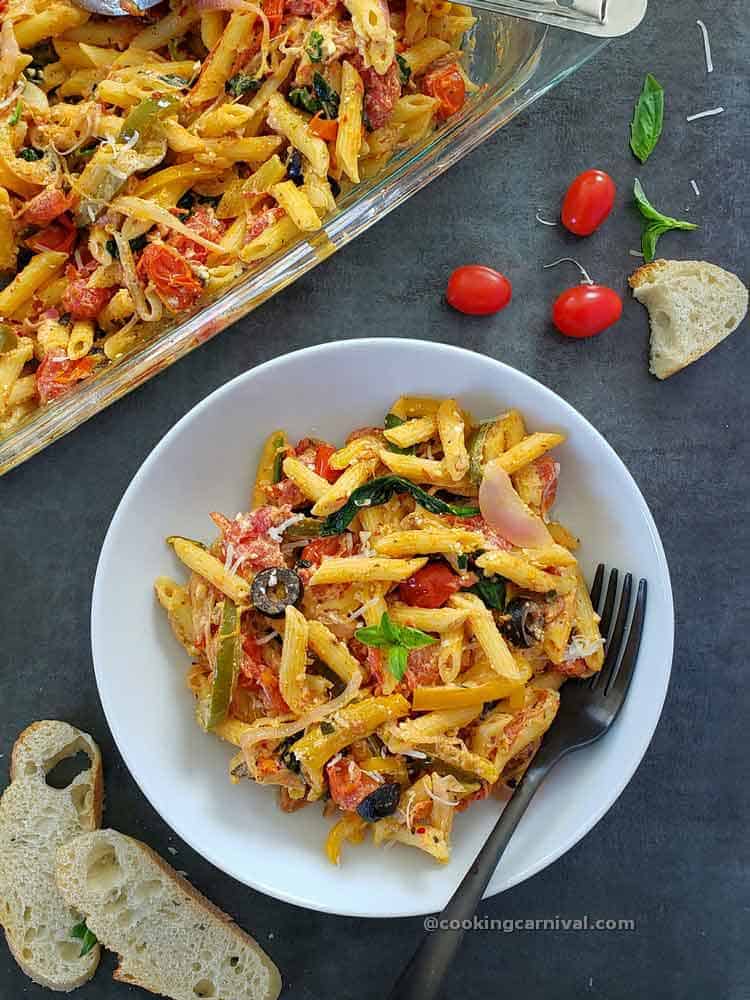 Baked feta pasta in a white bowl, fork and bread on the sides