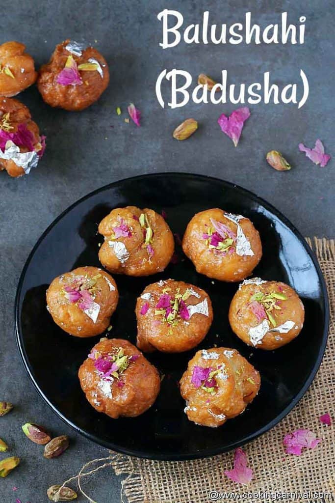 Pieces of balushahi garnished with nuts, silver vark and rose petals in a black plate