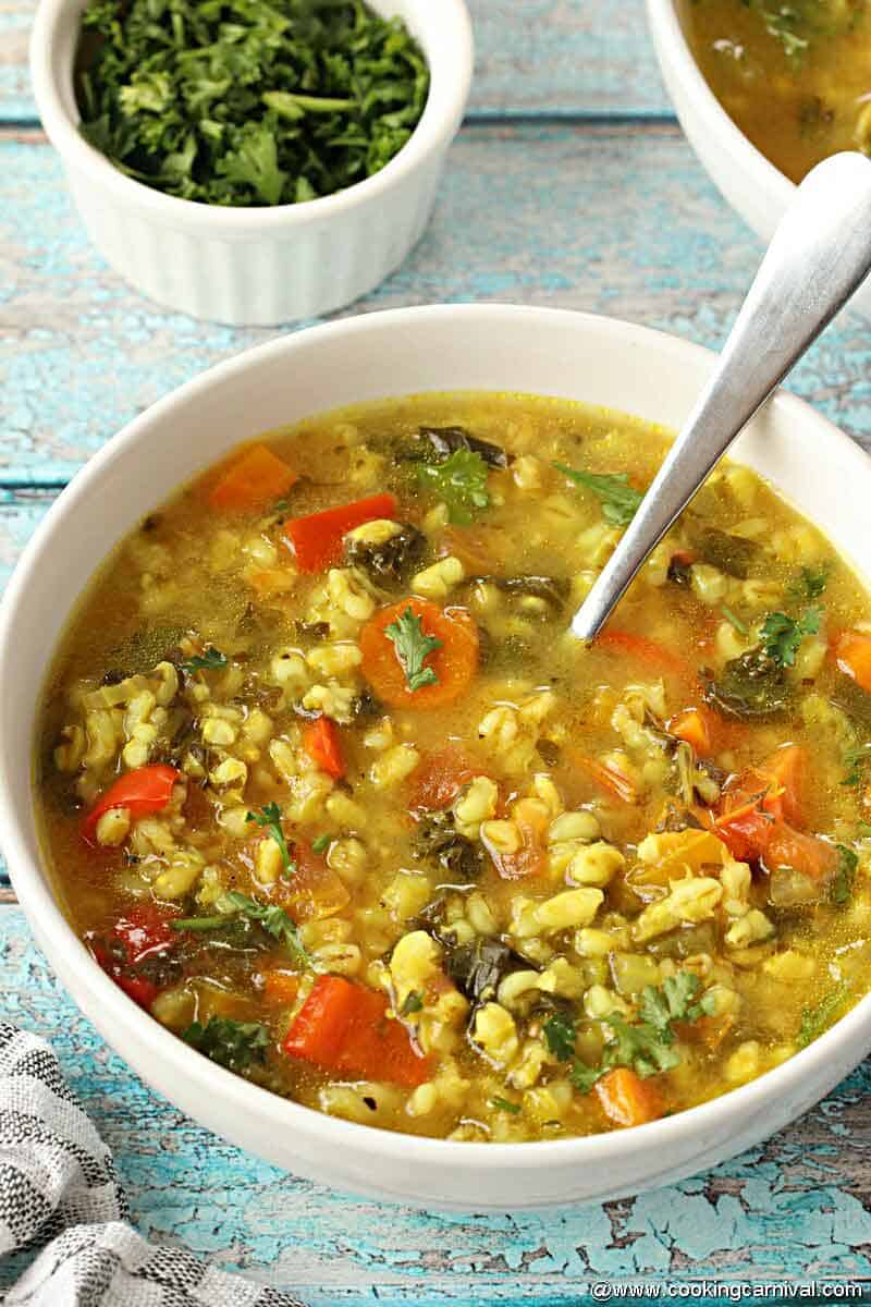 Vegetable barley Soup in white bowl with spoon