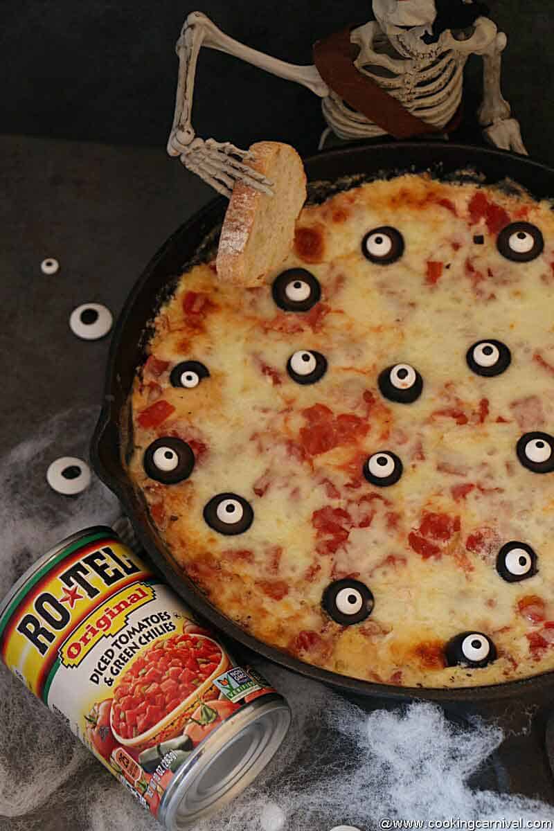 Halloween themed Pizza dip baked in a cast iron pan, Rotel tomatoes can on the sides