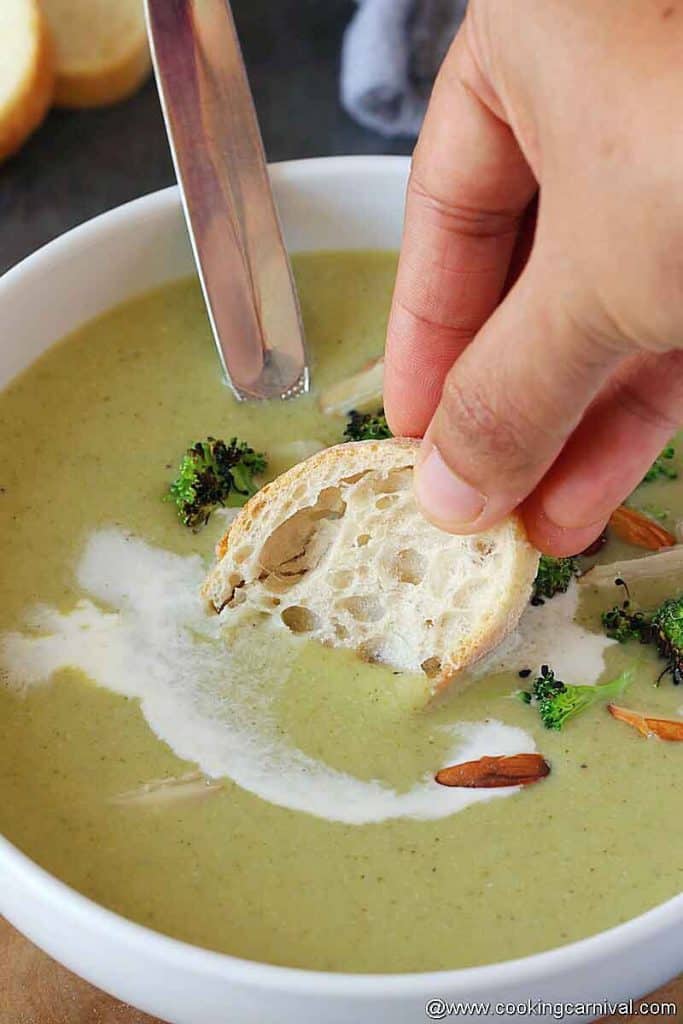 dunking crusty bread in creamy broccoli almond soup