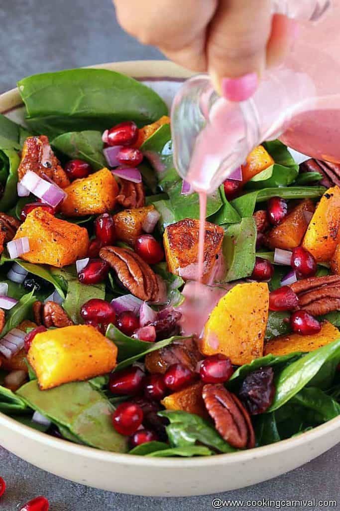 adding pomegranate vinaigrette on a spinach butternut squash salad