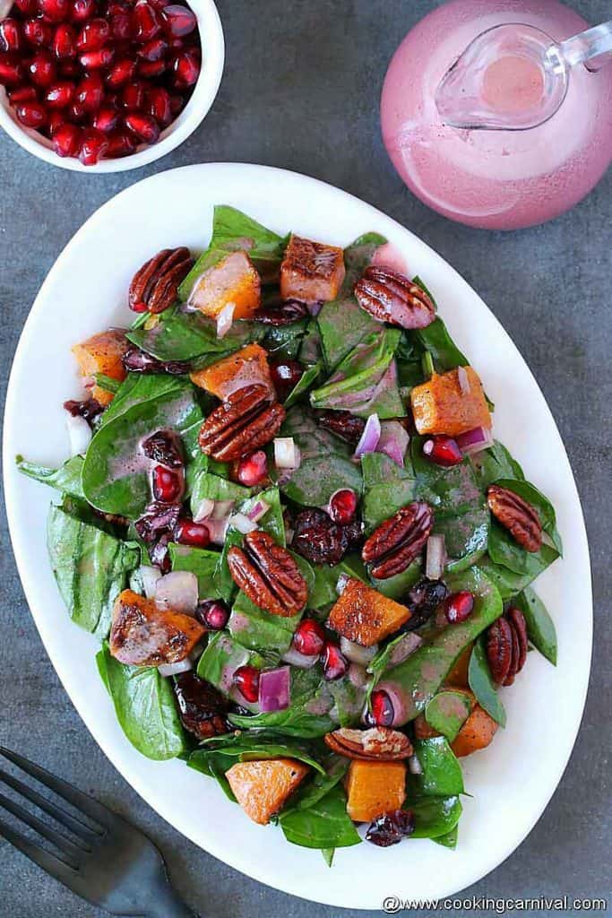 Butternut squash spinach salad with pomegranate vinaigrette on a white plate