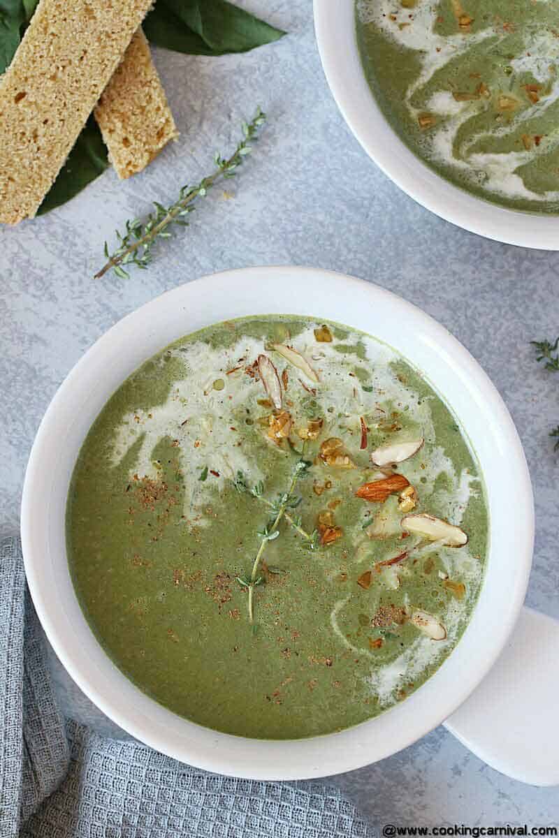 Spinach Soup in white bowl, garnished with sauteed garlic, almonds and cream