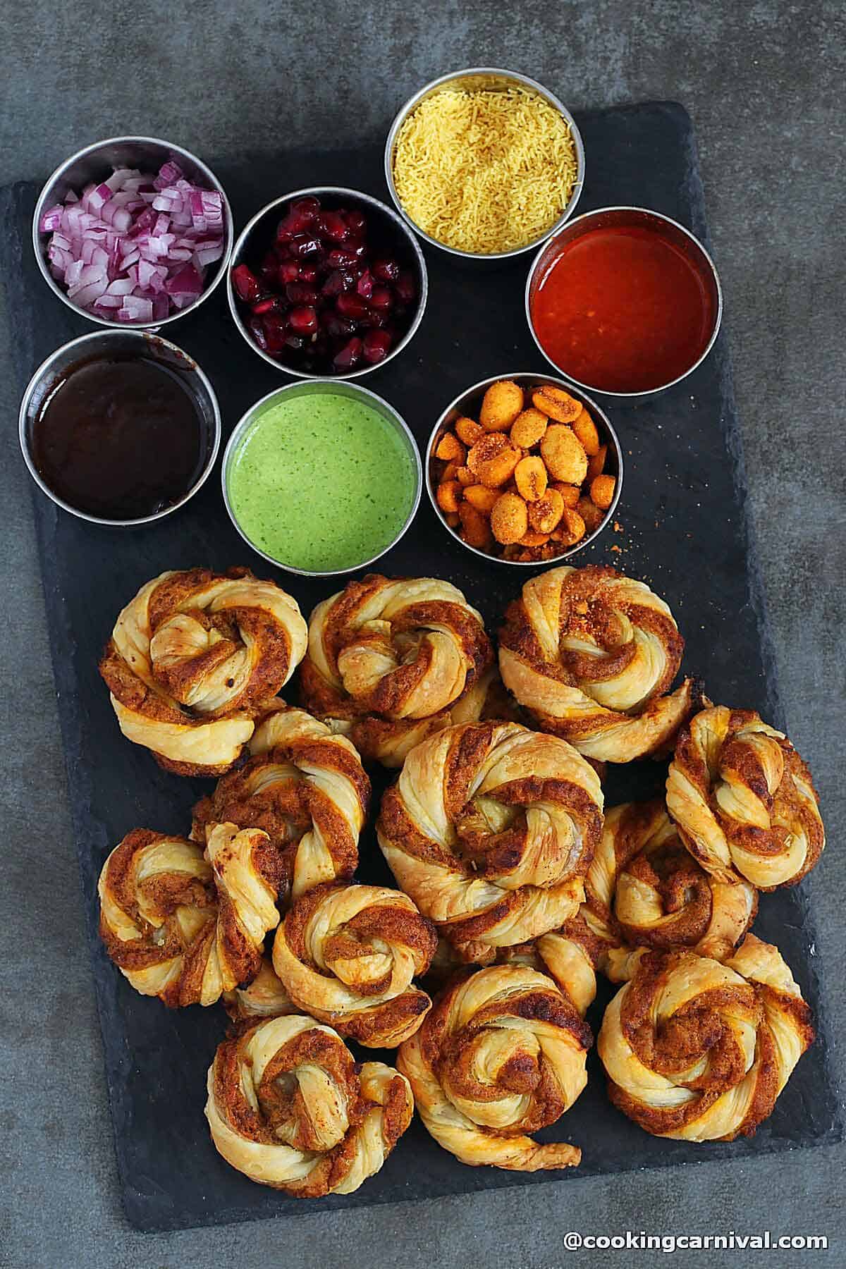 Dabeli bites on a black board, sweet, green and garlic chutney, sev, onion, masala peanut on a side.