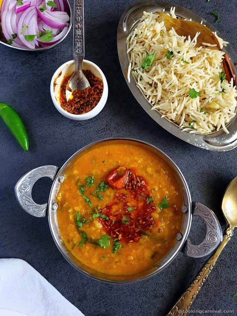 Dal tadka in steel bowl, jeera rice and onion on the sides