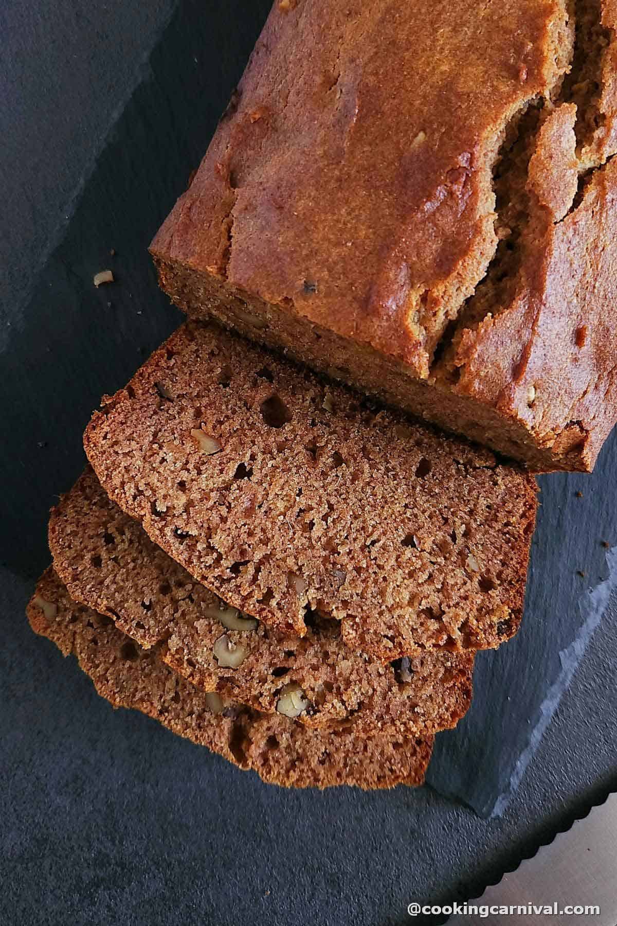 slices of eggless whole wheat dates and walnut cake on a black slat. 