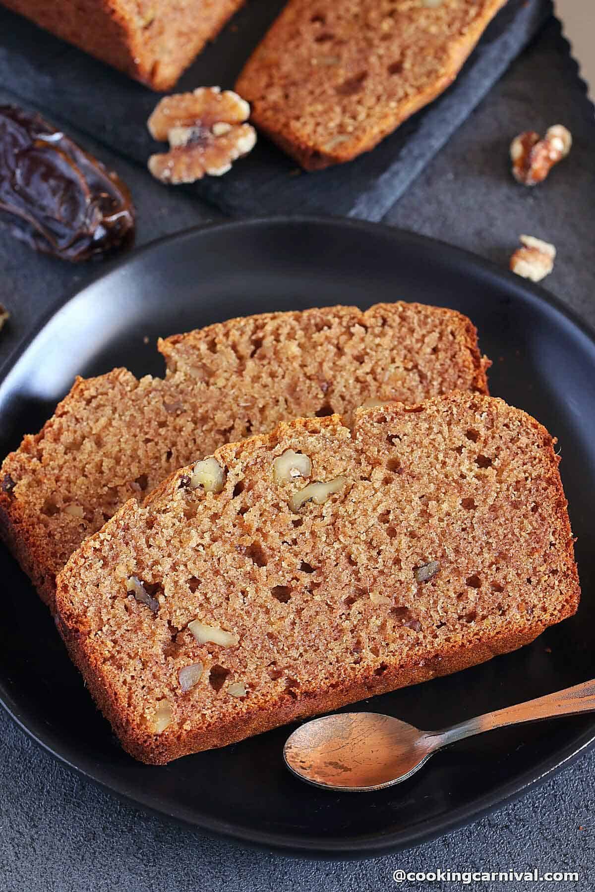 slices of eggless date and walnut cake on a plate with spoon.