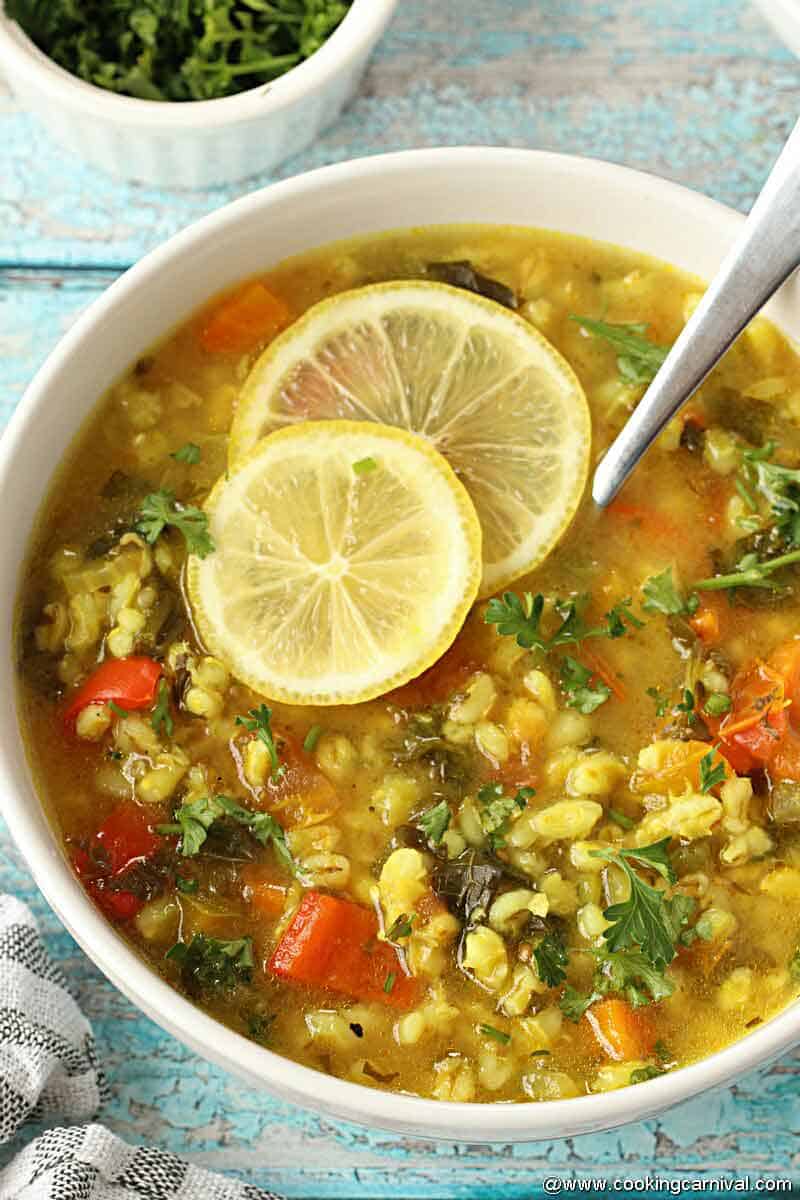 Easy vegetable barley soup in white bowl garnished with lemon slices and parsley