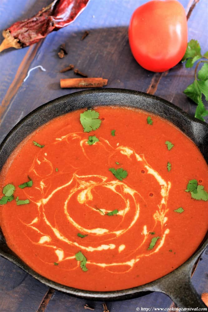 Makhani Gravy in a cast iron pan with tomatoes, red dried chilis, cilantro, cloves and cinnamon