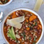 Instant Pot 15 beans soup in a white bowl, Parmesan cheese and avocado slices on top, crusty bread on the side