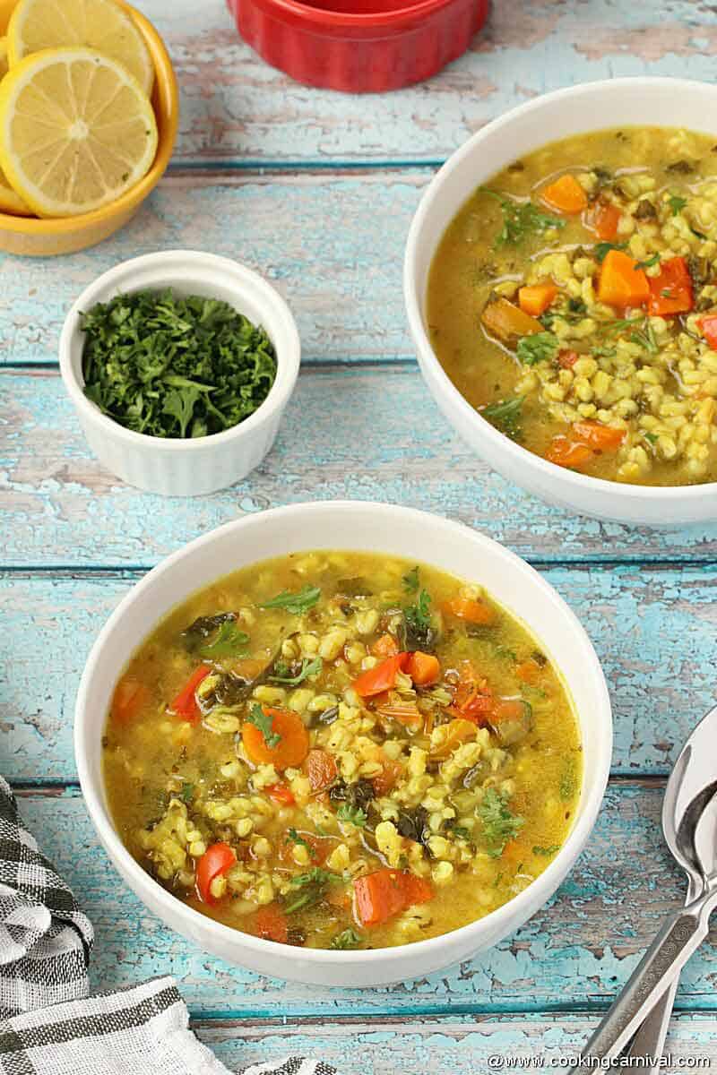 Vegetable Barley Soup in white bowl on blue rustic backdrop