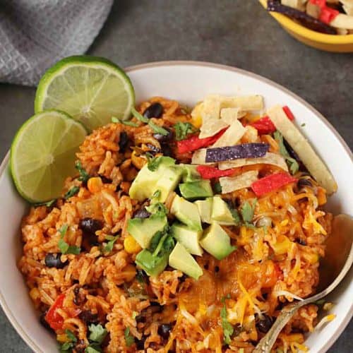 Meican rice in white bowl with spoon and topped it up with avocado, chips and cilantro.