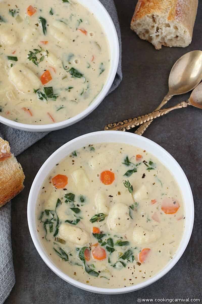 2 bowls of gnocchi soup, 2 kansa spoons and sour dough bread on the side.