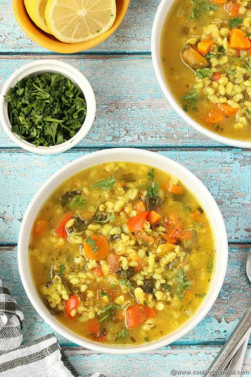 Vegetable Barley Soup in white bowl on blue rustic backdrop