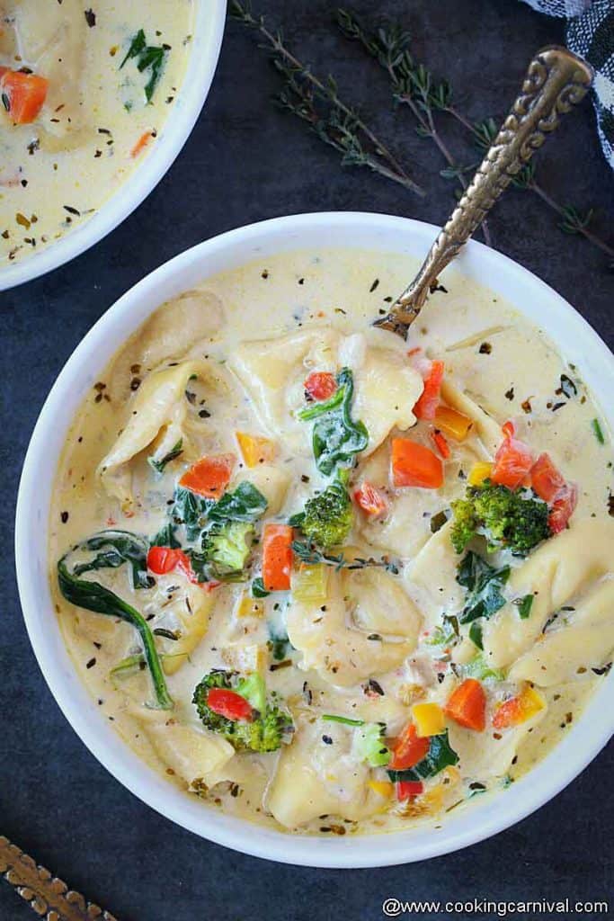 creamy tortellini soup in white bowl with spoon