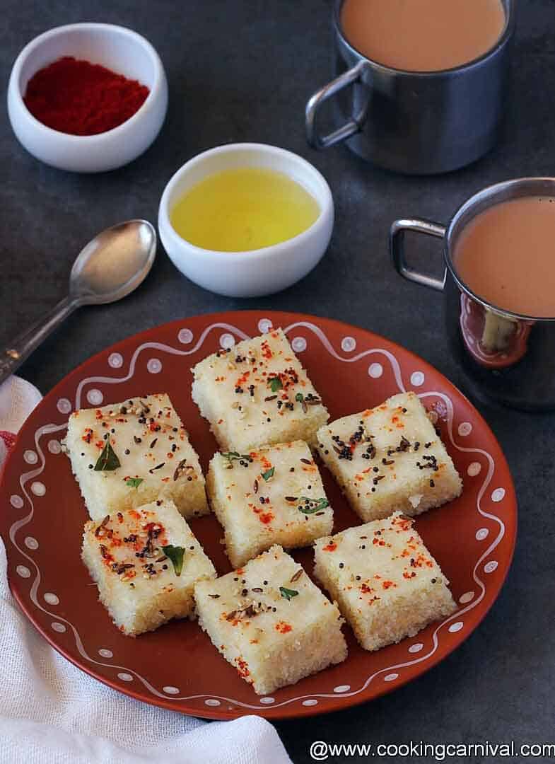 Dhokla on a traditional plate, tea, oil and chili powder in sides