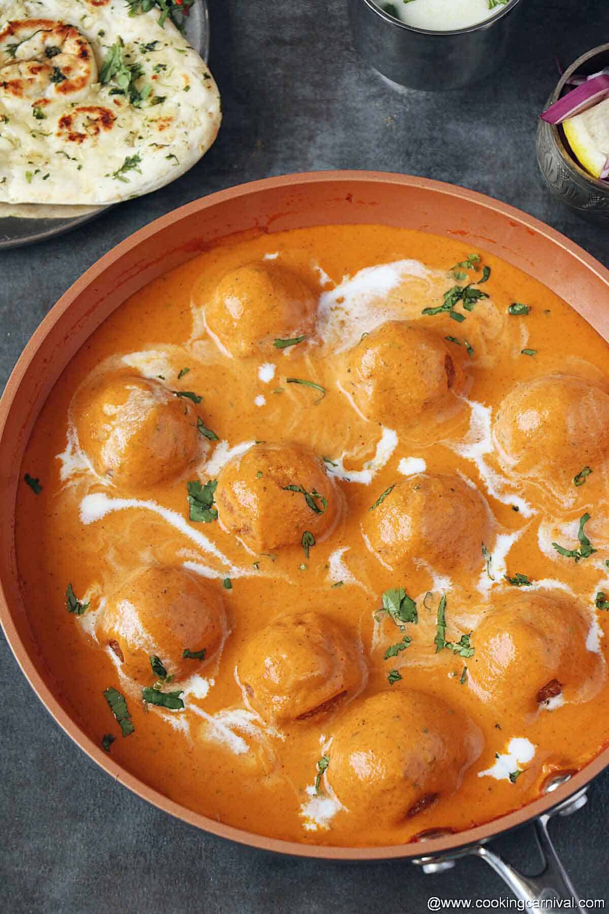 Malai kofta garnished with cream and cilantroin copper pan