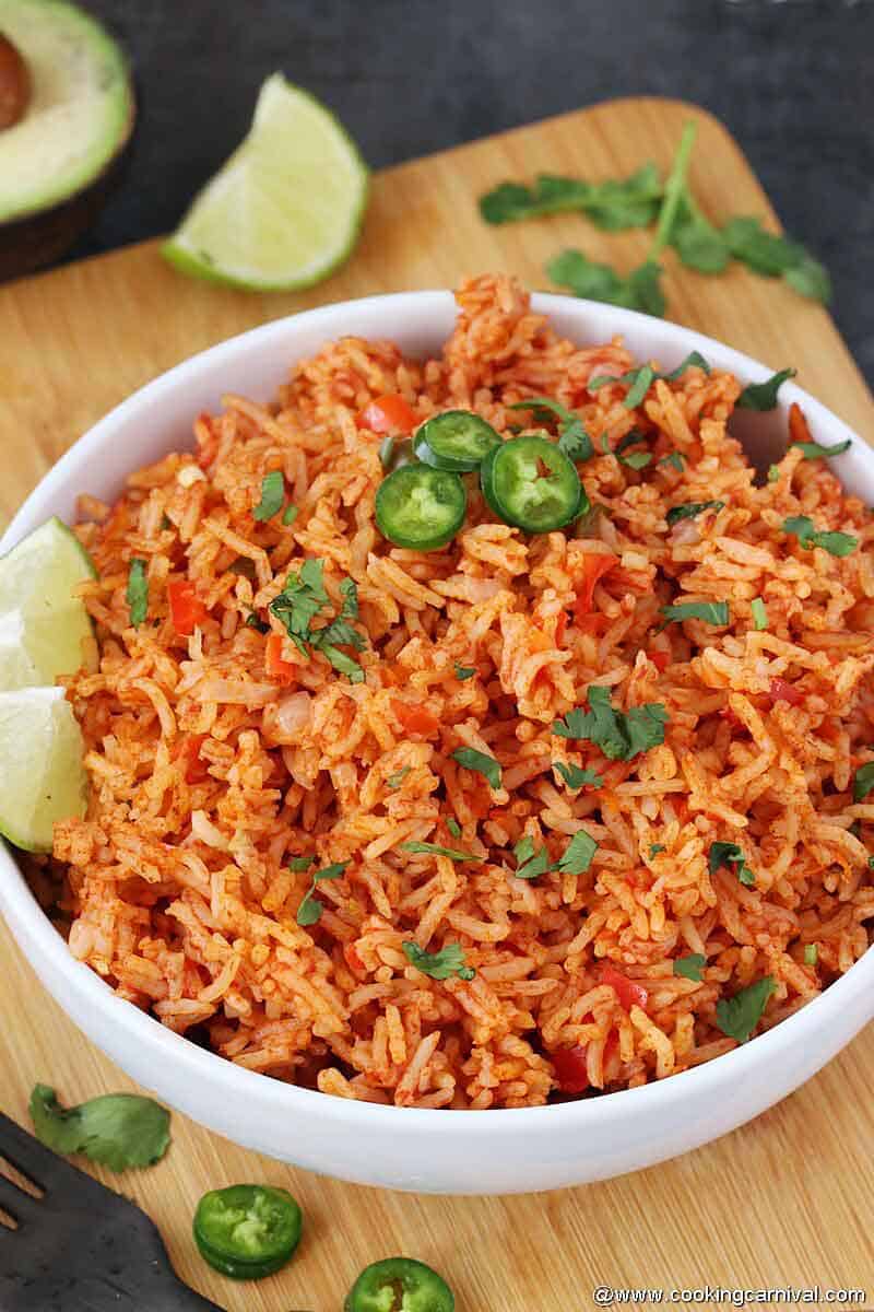 Mexican rice in white bowl with lime wedges and jalapenos