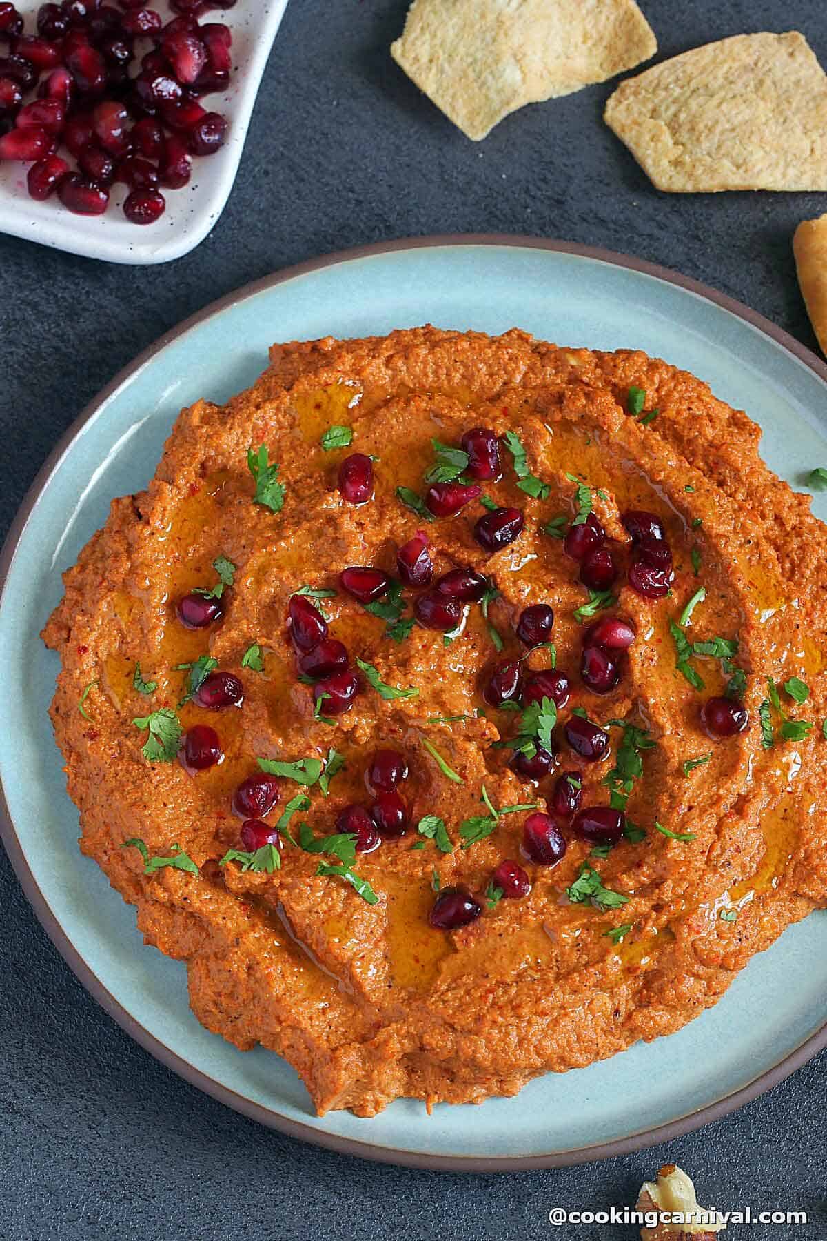 Muhammara dip on a plate garnished with pomegranate and parsley. 