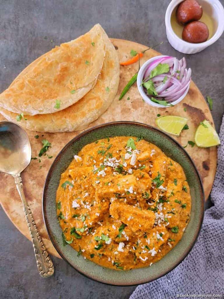 Paneer lababdar in a bowl, paratha, onion, green chilies and lime on the side