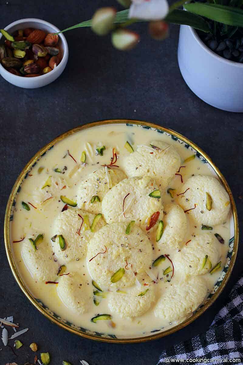 Bowl full of Indian dessert rasmalai, nuts on the side.