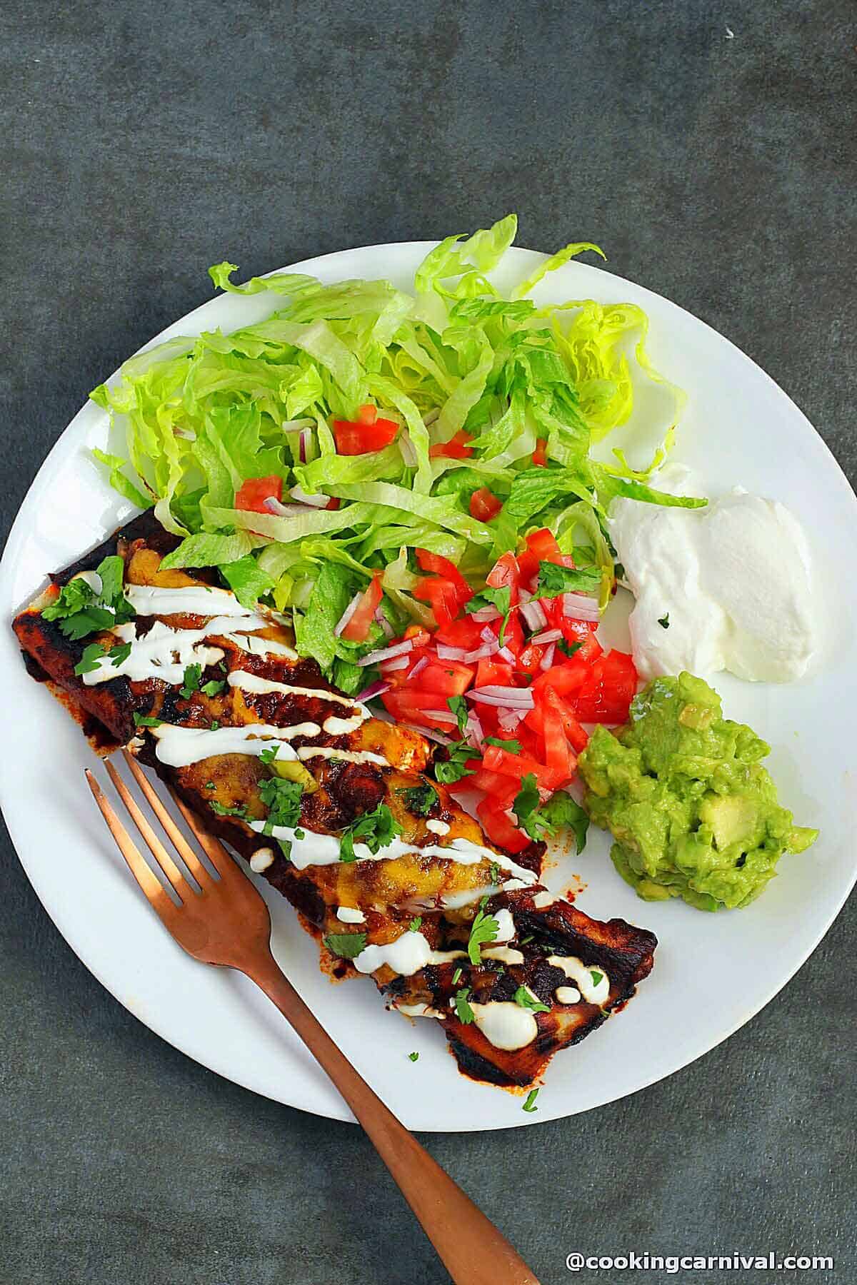 Vegetable Enchilada served in a plate with lettuce, sour cream, guacamole and salsa.