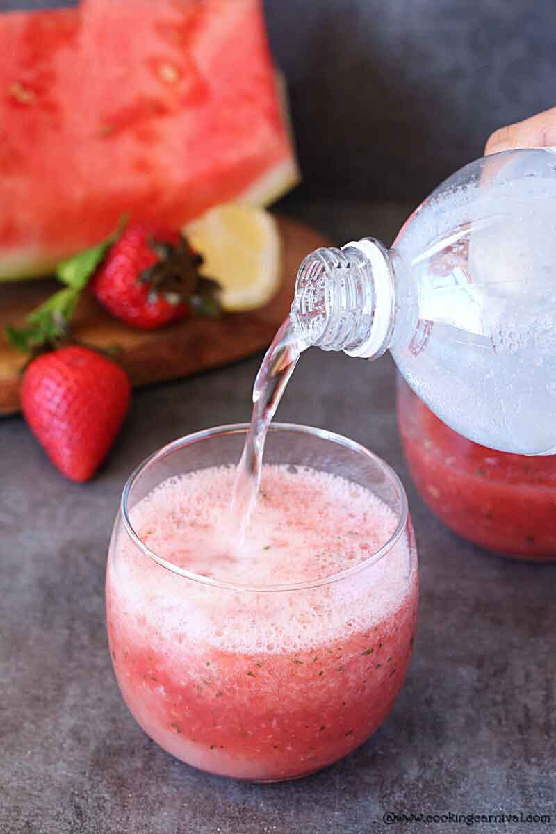 Pouring club soda in a glass of strawberry lemonade