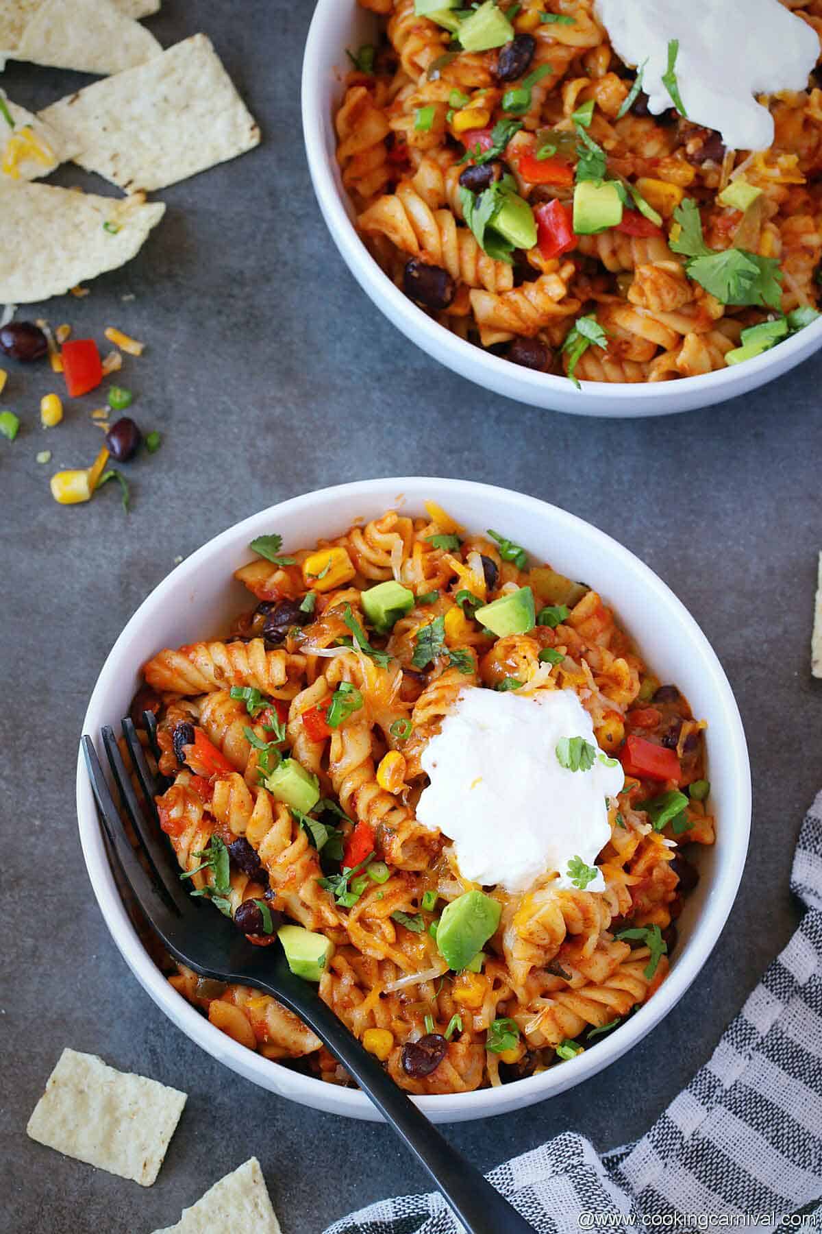 Taco pasta in 2 bowls garnished with sour cream, cilantro and avocado