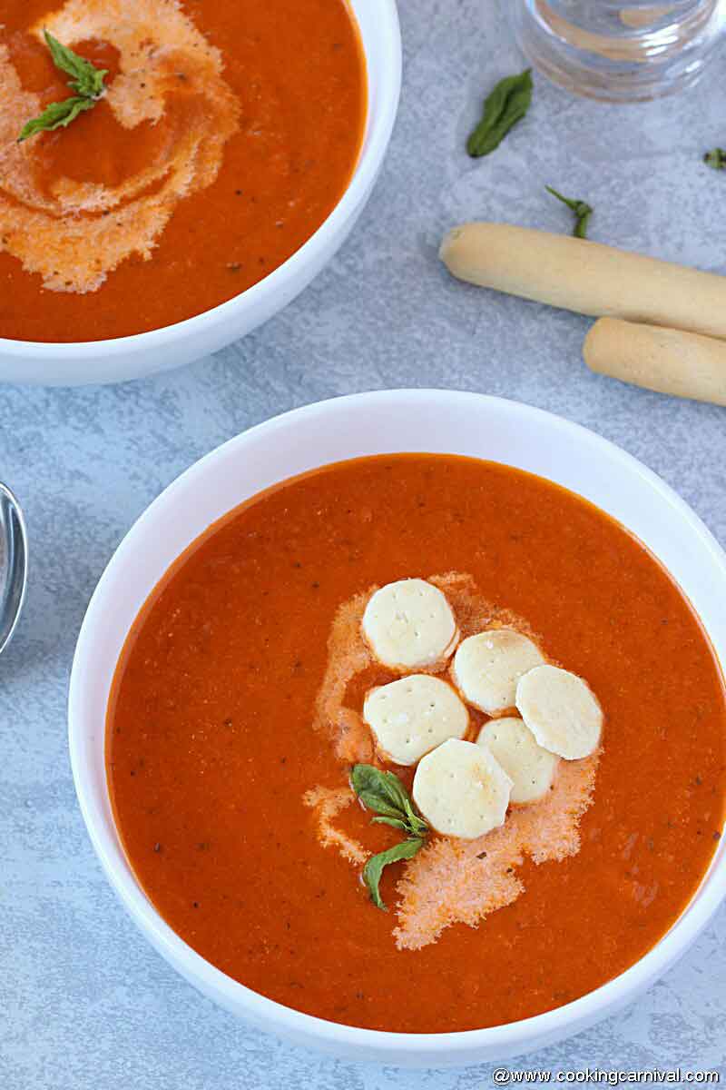 Instant pot tomato basil basil in a white bowl garnished with oyster crackers, basil leaves and cream