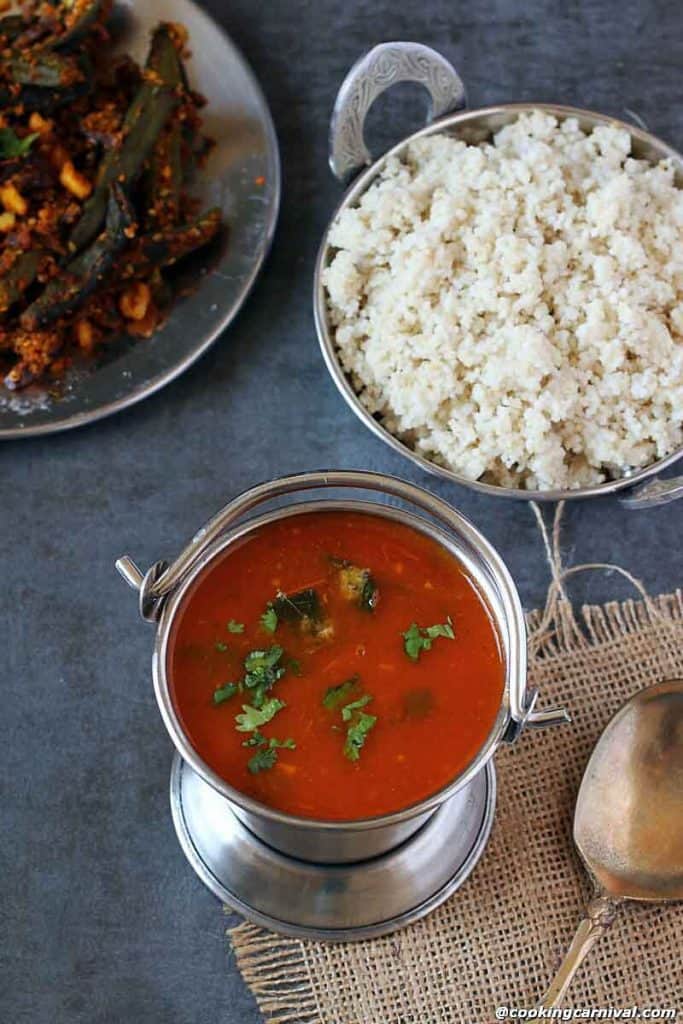 Tomato rasam in steel pot, barnyard millet on the sides