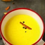 Golden milk in a big mug, garnished with cinnamon sticks and peppercorn