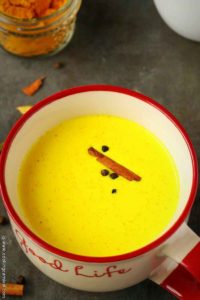 Golden milk in a big mug, garnished with cinnamon sticks and peppercorn