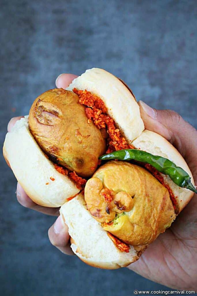 holding 2 vada pav with fried green chilies