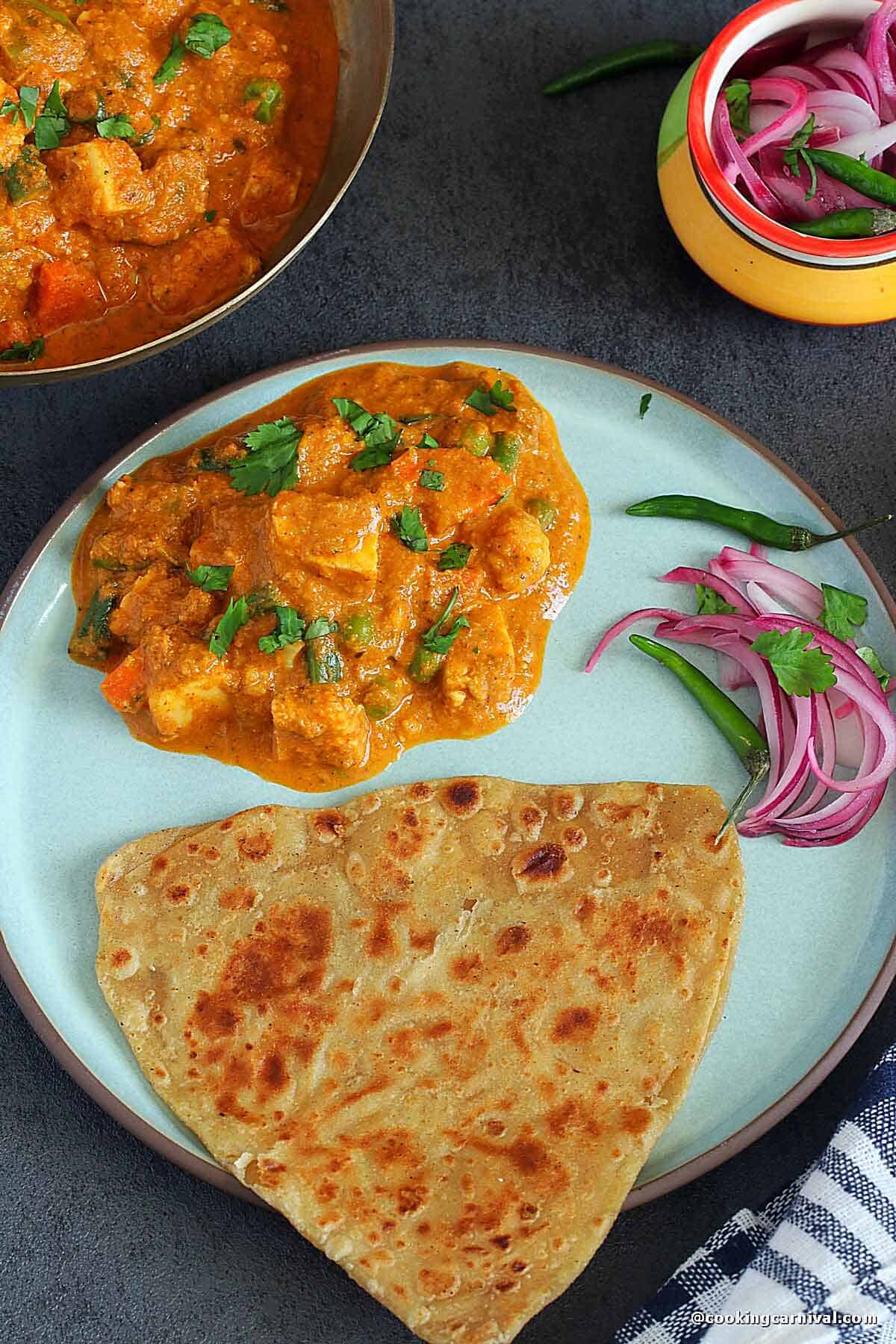 Veg maratha served in a ceramic plate with plain paratha, onion and green chili.