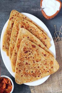 4 parathas in a white plate, pickle and curd on the sides