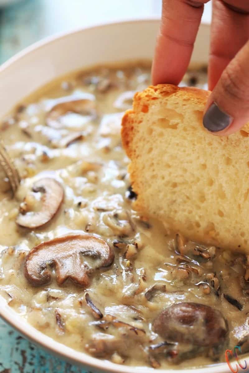 Dipping bread slice in Vegan Wild Rice Mushroom Soup