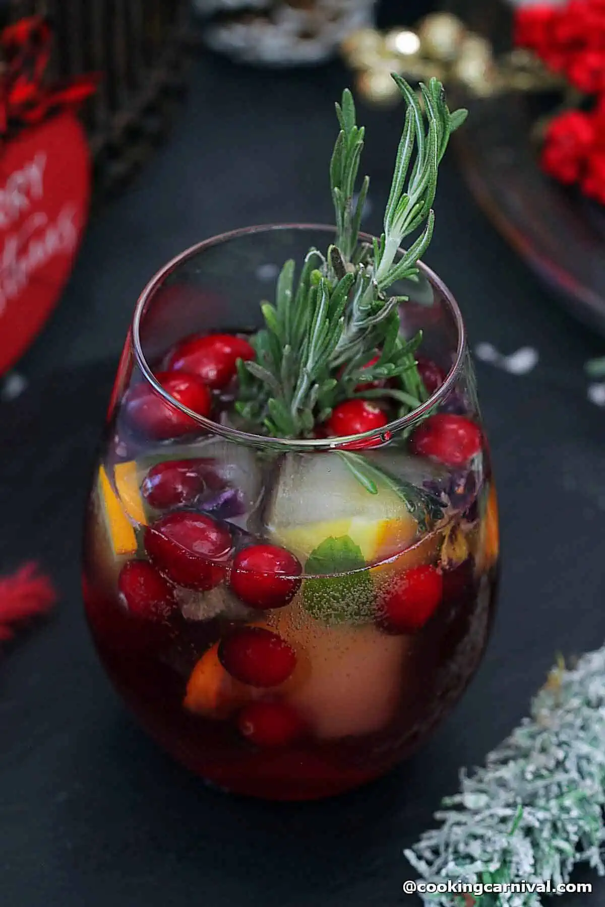 basil cranberry mocktail in a glass, garnished with rosemary, and holiday ice cubes.  