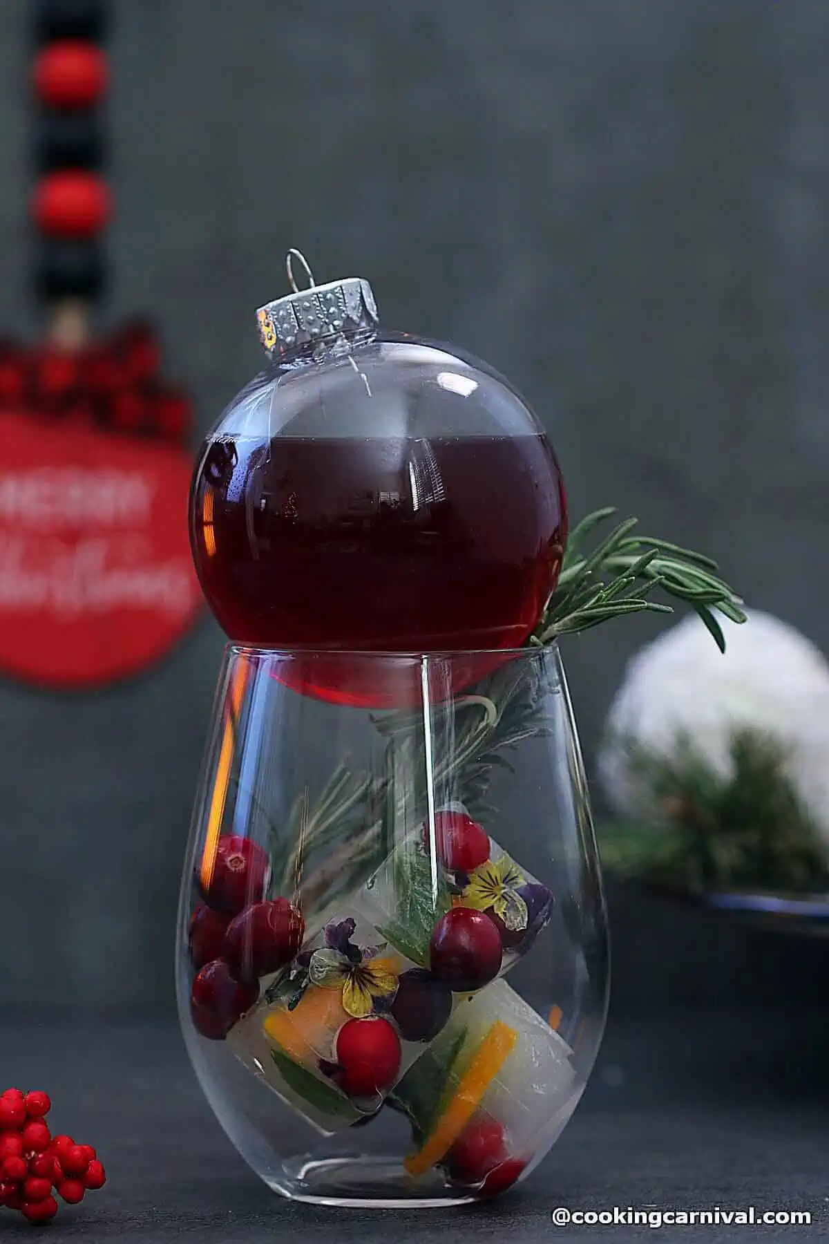 Mocktail filled in clear glass ornaments and served in a glass with holiday ice cubes, rosemary, and cranberries. 