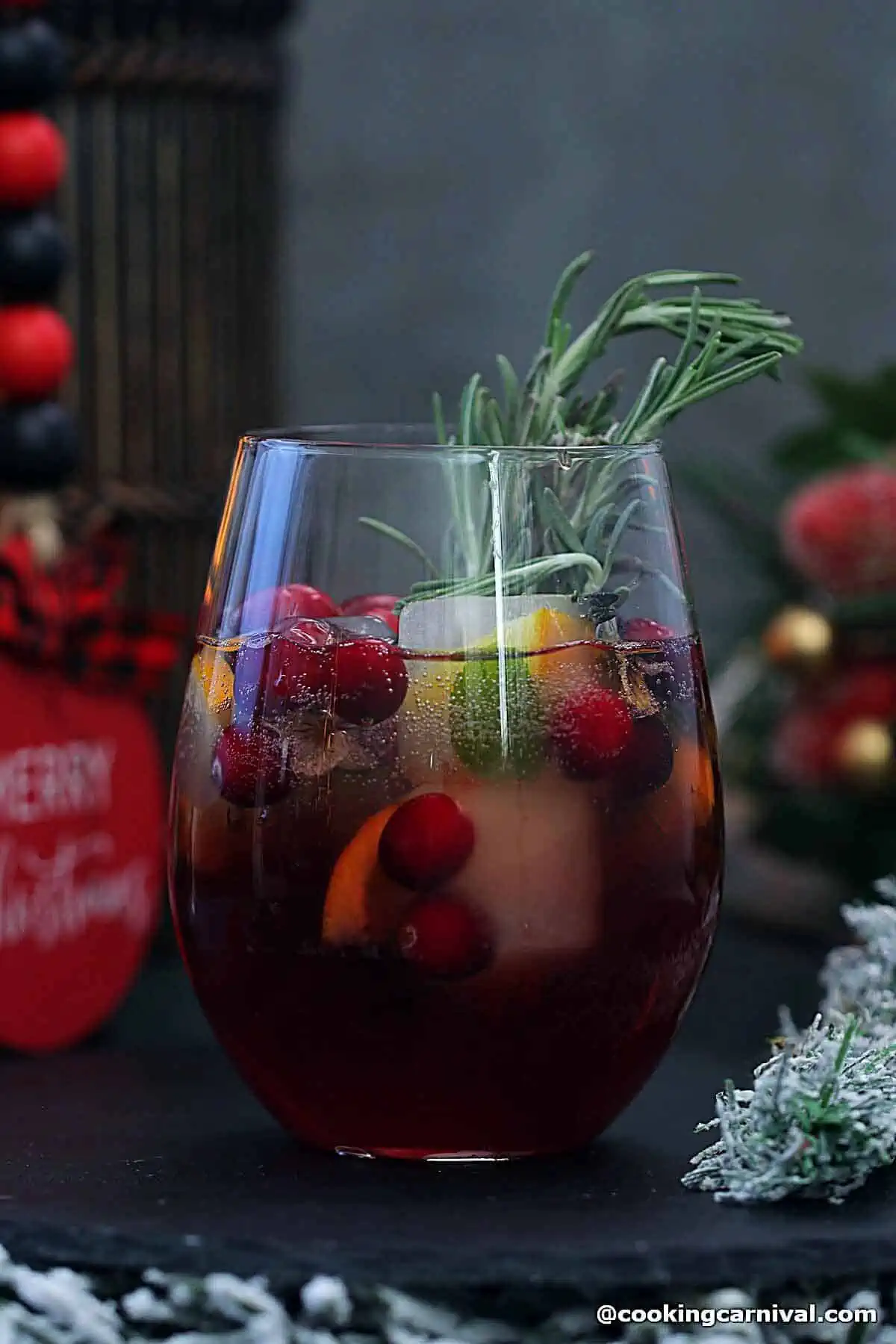 Basil cranberry mocktail in glass, garnished with holiday ice cubes, cranberries, and rosemary.