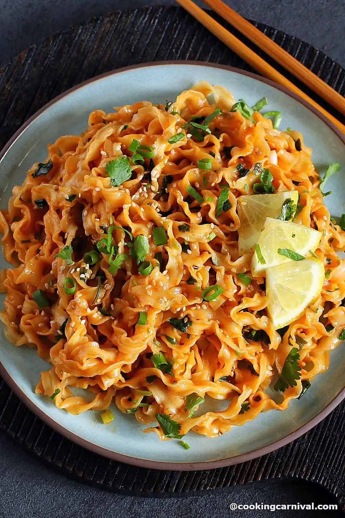 Gochujang noodles on a plate, topped with cilantro and lemon. 