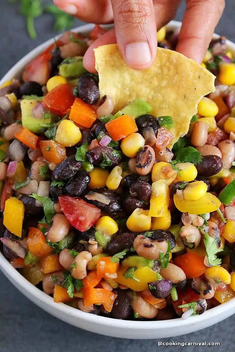 take a bite of cowboy caviar with tortilla chips from white bowl.