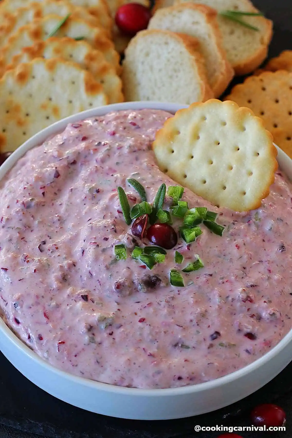 Dipping crackers in a bowl filled with jalapeno cranberry dip.