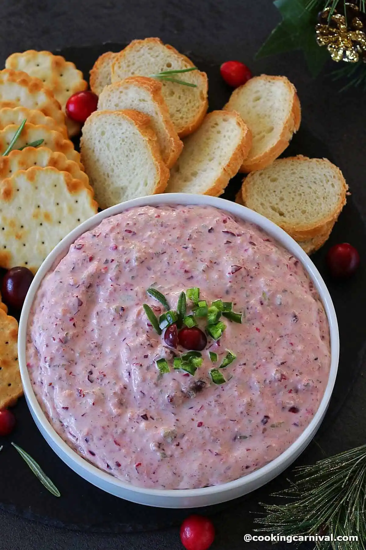 Cranberry Jalapeno dip with cream cheese in a white bowl, crackers, and crostini on the sides.