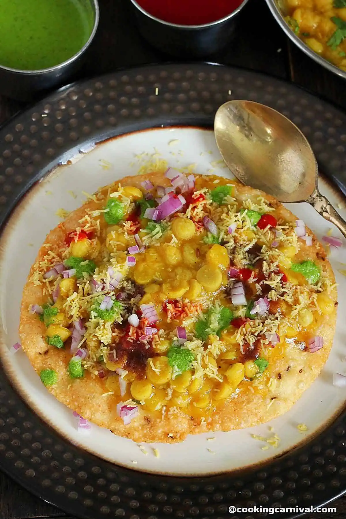 Dal Pakwan served in a plate, topped with sweet chutney, green chutney, garlic chutney, sev and onion.