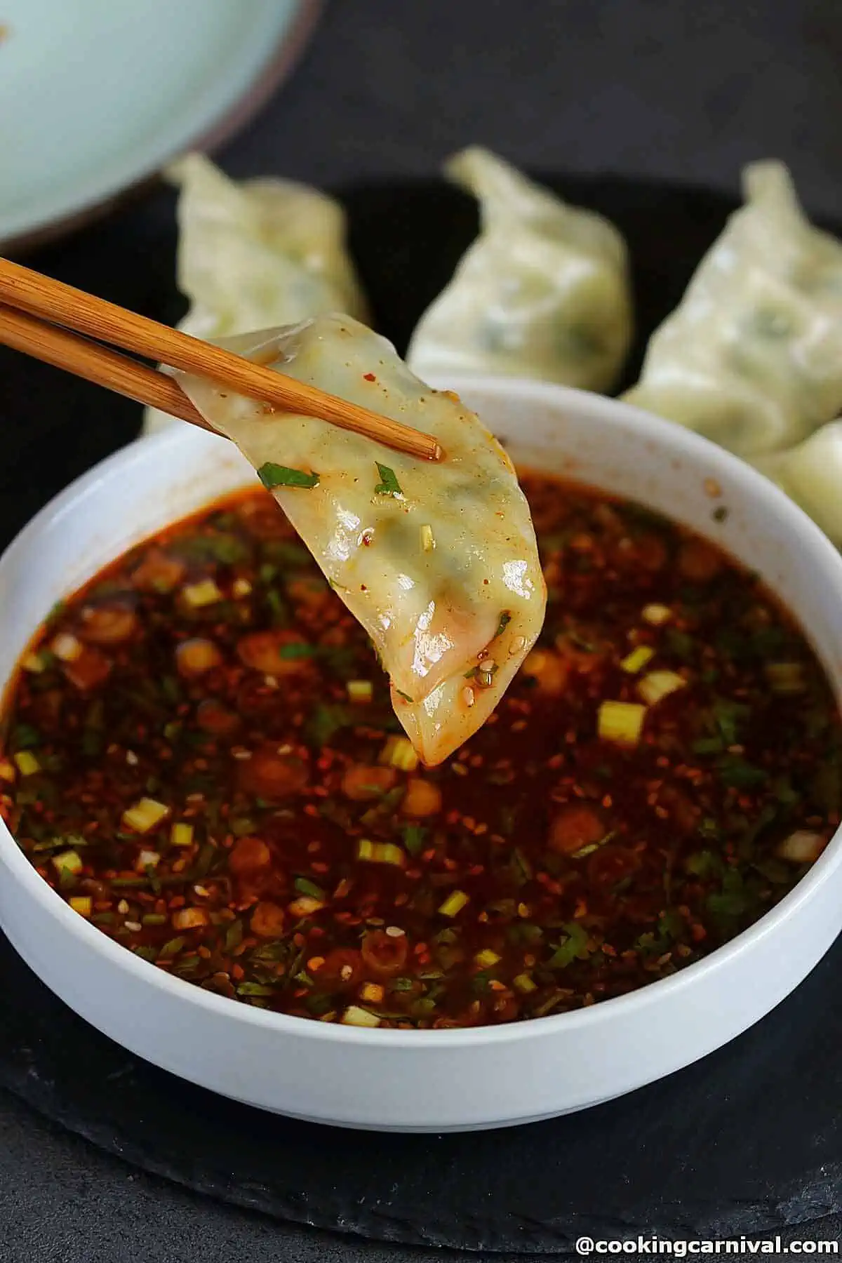 Dumpling dipped in sauce and held with chopsticks. 