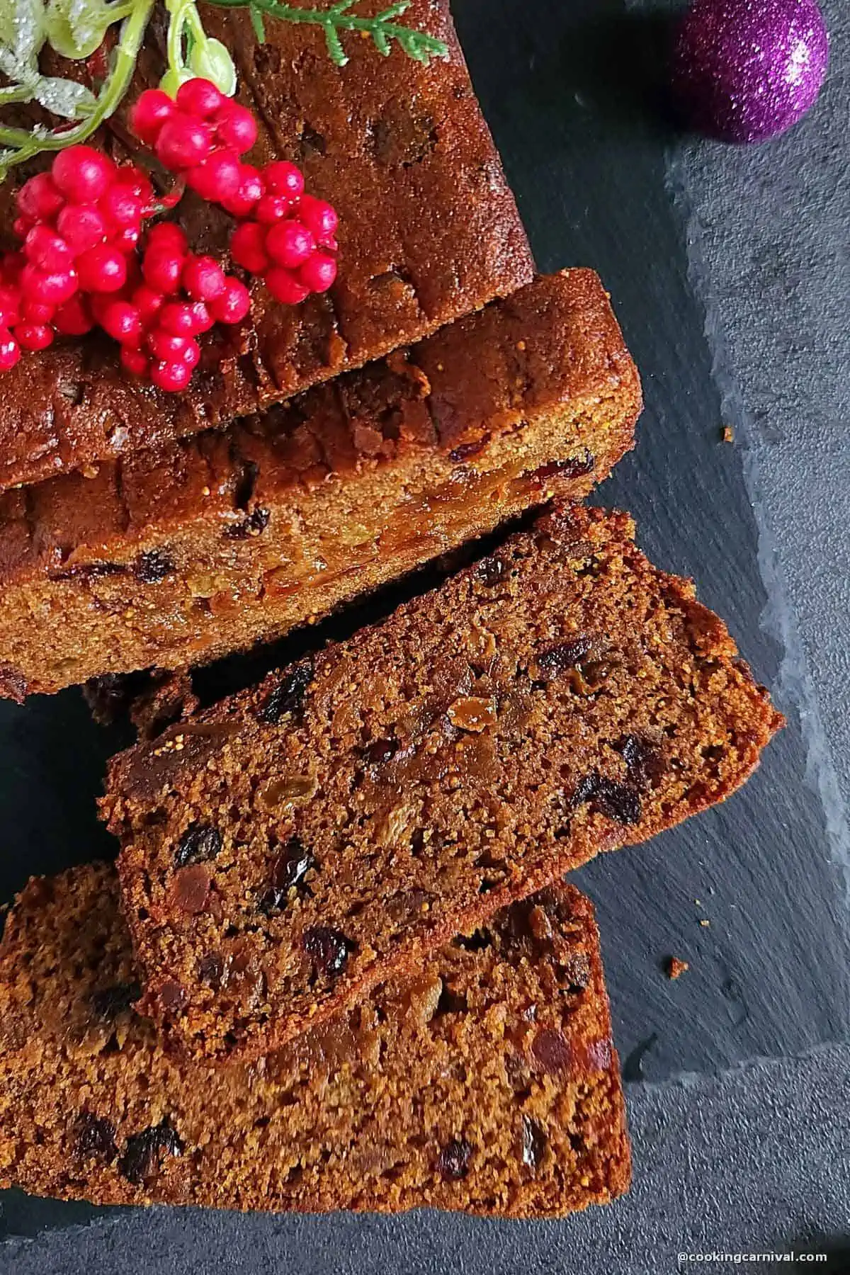 Sliced eggless fruit cake on a black slate.